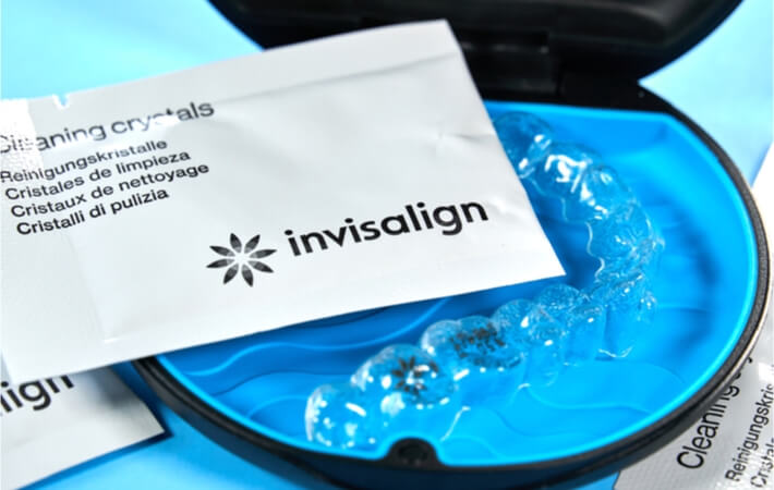 A pair of aligners sitting in their case with a packet of cleaning crystal laid on top of them.