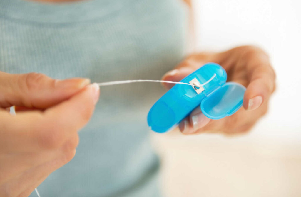 A woman pulls out a strand of floss from its blue container.