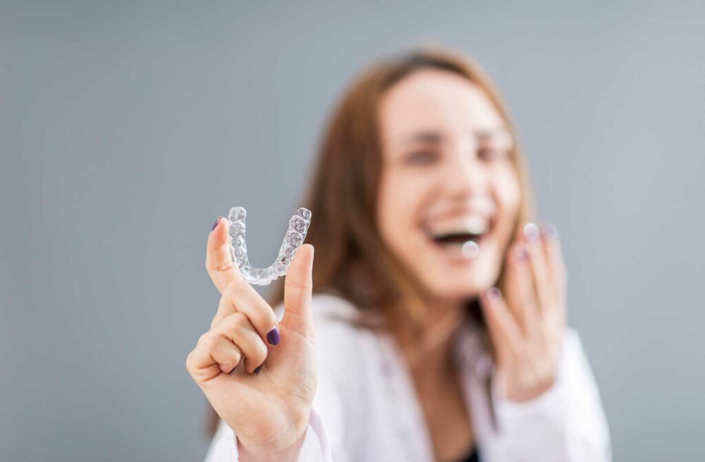 Woman laughing while holding up her Invisalign aligner.