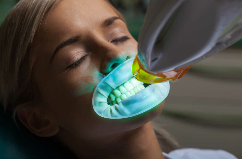A woman is sitting on a dental chair and getting her teeth whiten at a dental clinic