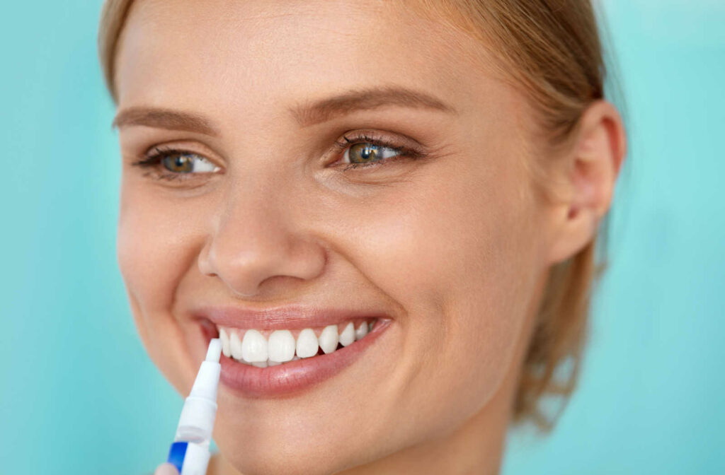 A close-up of a woman using a whitening pen to whiten her teeth.