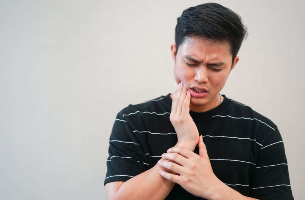 A young man in a black shirt with a white thin stripe is pressing his right cheek above his jaw in severe pain due to an impacted wisdom tooth that may have an abscess.