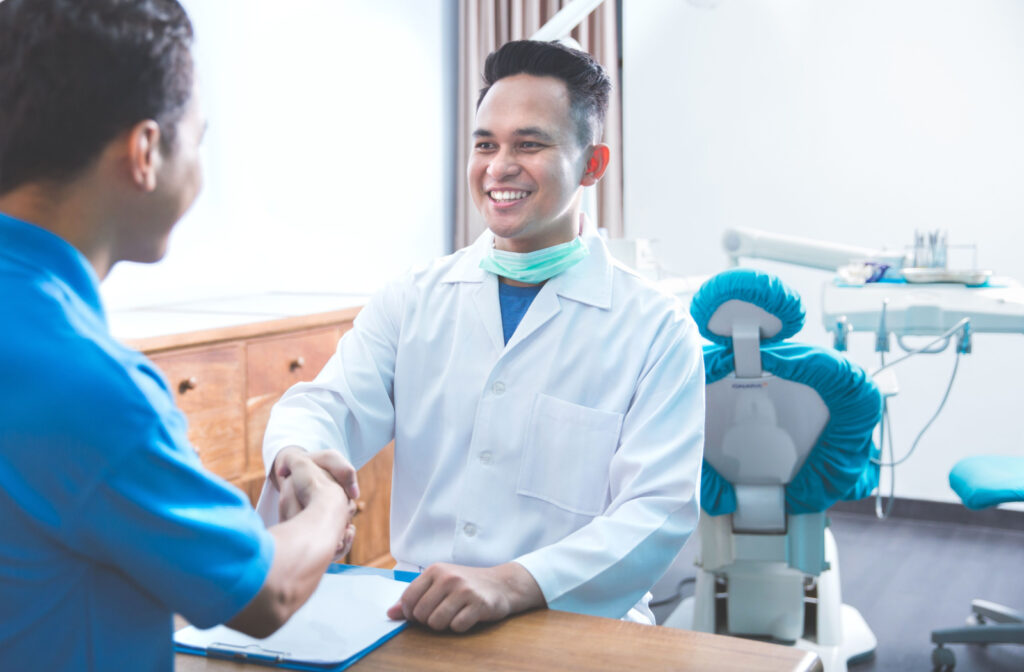 A man in an dentist's office shaking hands with his dentist.