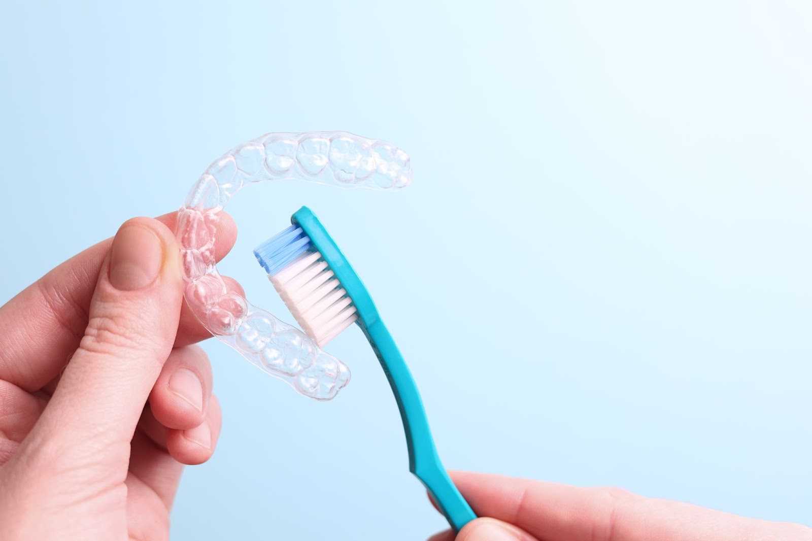 A close-up of someone cleaning their Invisalign with a soft toothbrush.