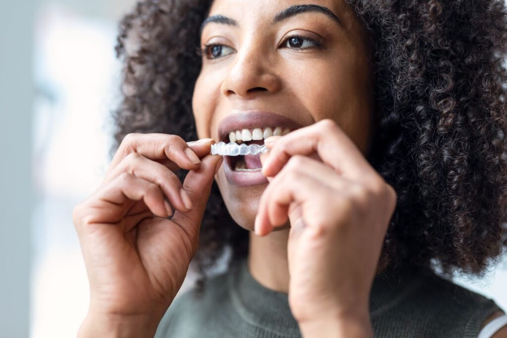 A young woman putting her Invisalign aligners on her teeth.