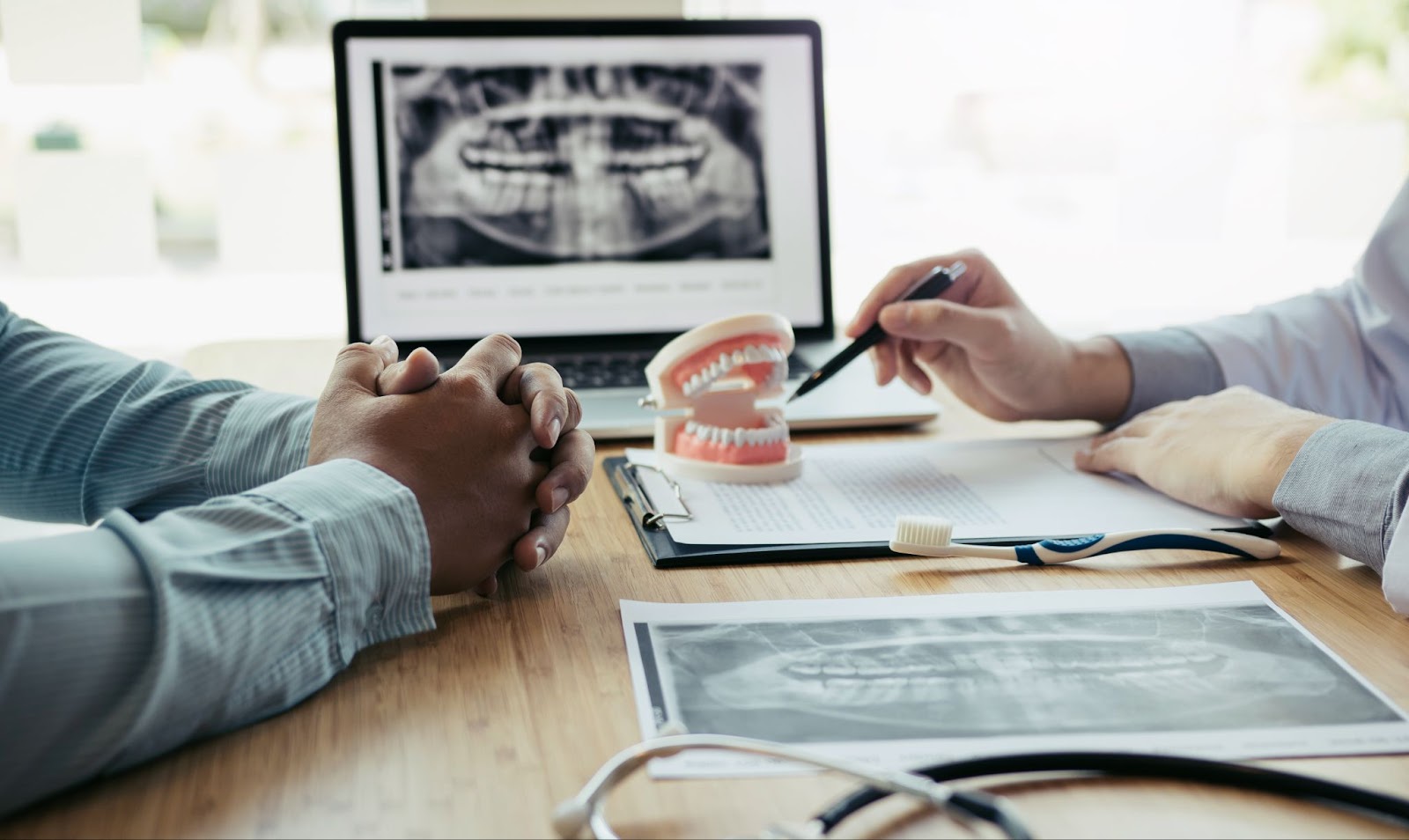 A dentist points at a model of teeth and discusses oral health with their patient