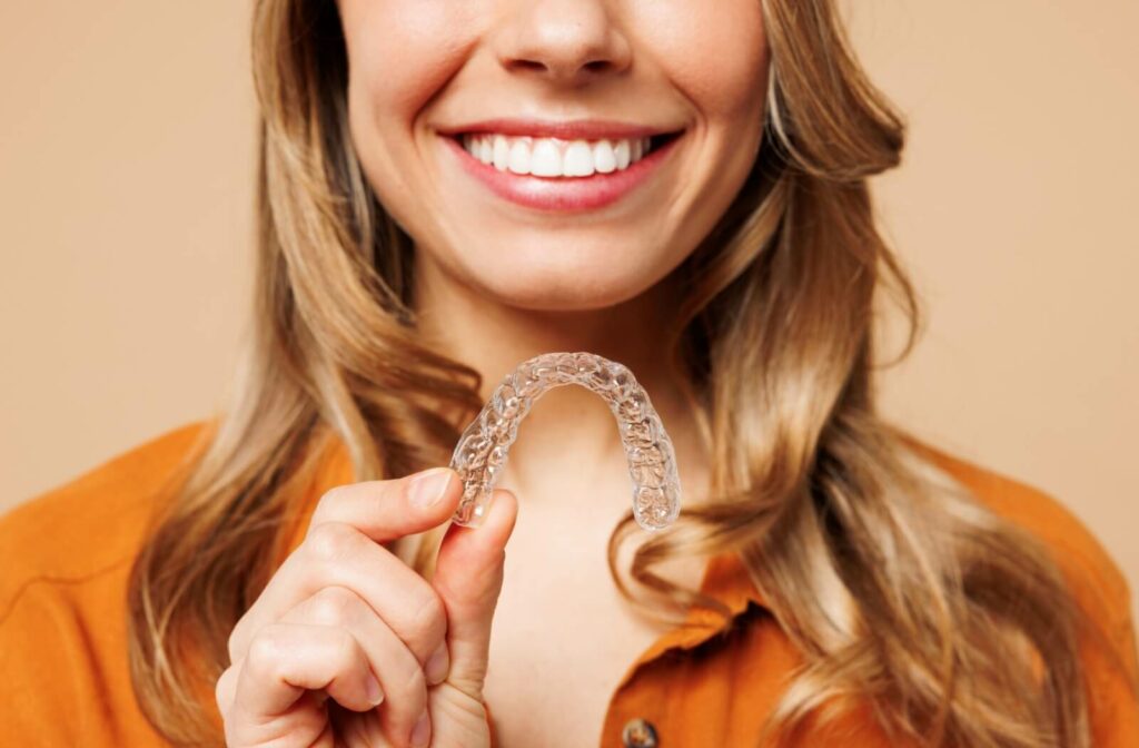 A close-up image of a smiling lady holding up her Invisalign clear aligners.