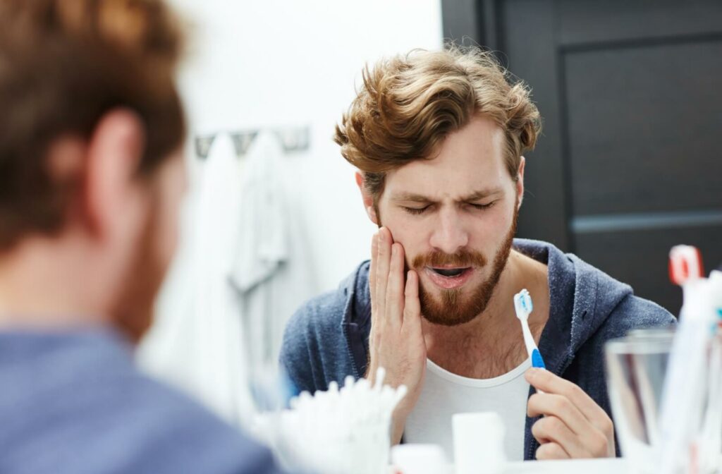 A man holding his toothbrush in one hand and his jaw in the other, with a pained expression on his face.