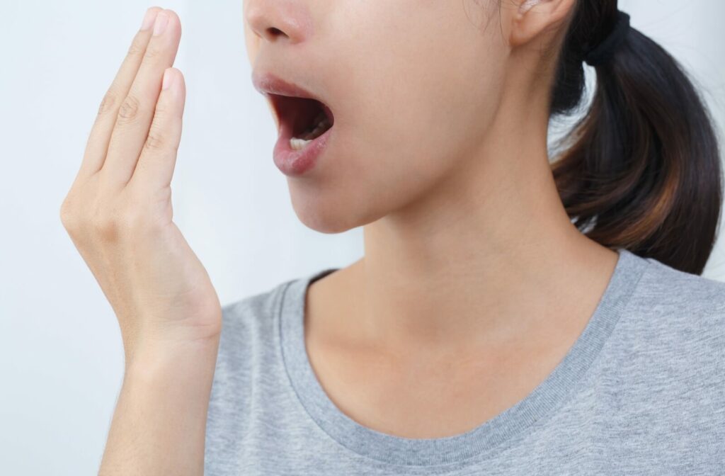 An adult cups their hand in front of their mouth to smell their own breath.