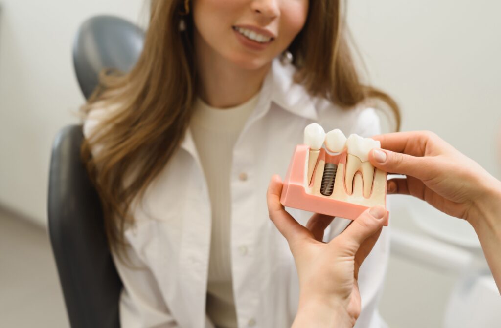 A dentist holds an implant model while discussing dental implants with a patient.