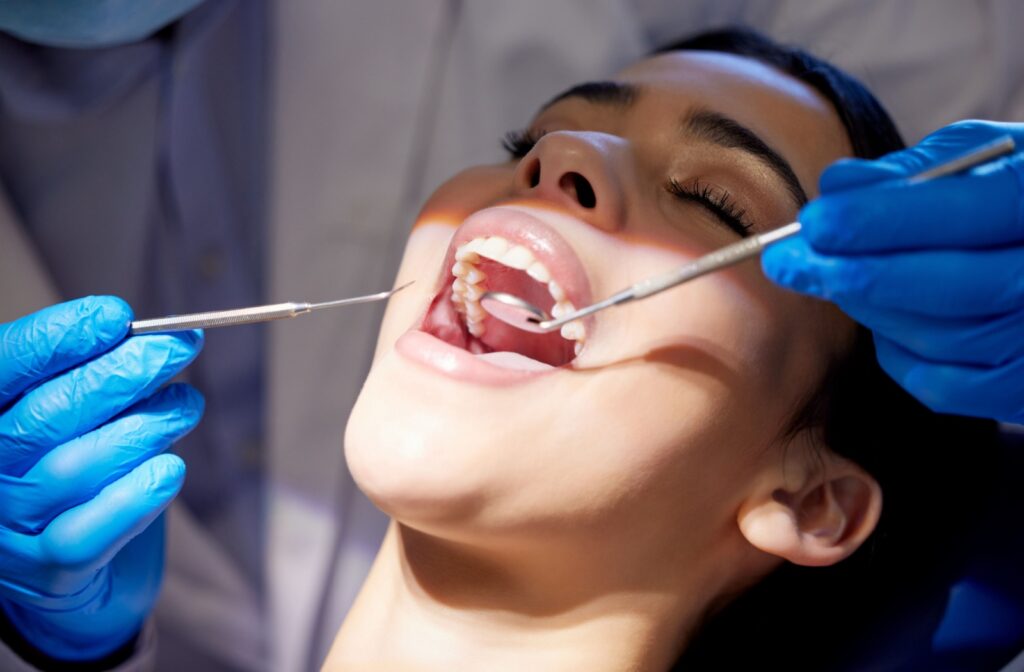 Close-up of a dental professional cleaning a patient’s teeth with metal tools.