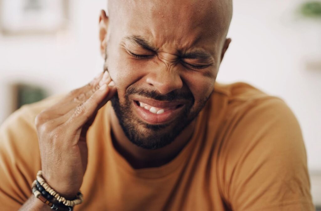 A man wincing and holding the side of his face in pain, implying tooth pain.