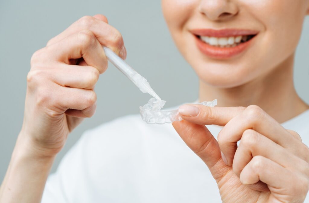 Young woman applying a home teeth whitening treatment with a tray and gel.